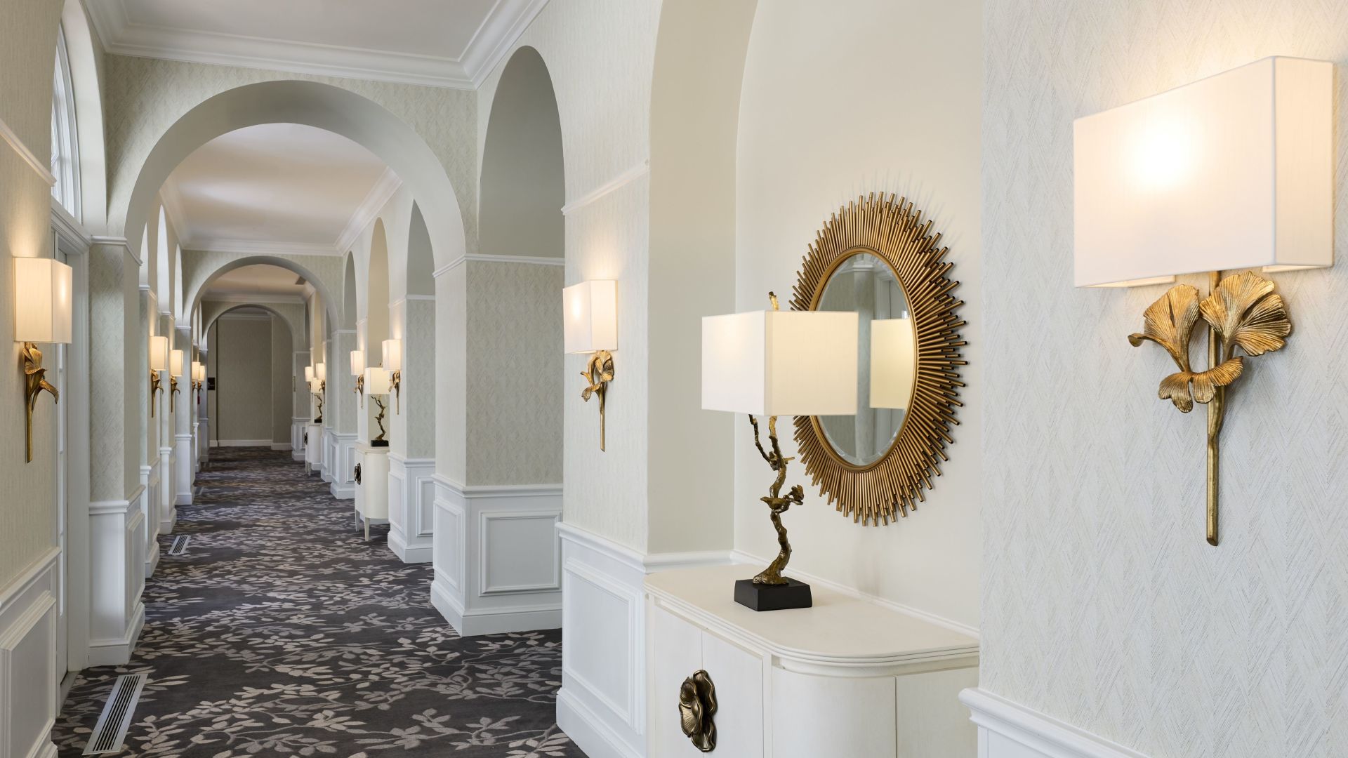 A Hallway With A Mirror And A Table With Lamps On It